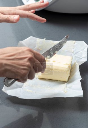 Schneiden von Butter auf Pergament, mit verstreuten Krümeln auf einer glatten grauen Arbeitsplatte.