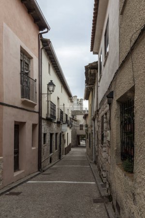 narrow, stone-paved street flanked by old, textured buildings under a cloudy sky in a historic town