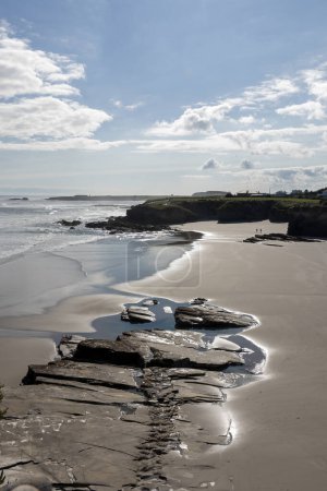 Une plage sereine avec des affleurements rocheux, des vagues calmes et un ciel nuageux reflétant la lumière du soleil magnifiquement