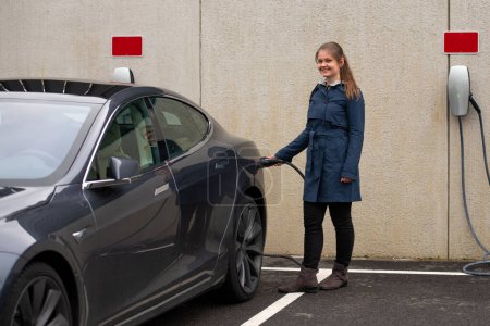 Glückliche hübsche junge lächelnde Frau lädt modernes Elektroauto