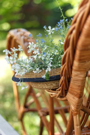 Téléchargez les photos : Chapeau de paille, fleurs blanches et une chaise en osier dans le jardin. Résumés - en image libre de droit
