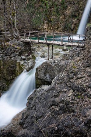 Blick auf den Balta di Stringa Wasserfall mit Holzbrücke in der Nähe des Dorfes Iliochori in der Gegend von Zagori in Epirus, Griechenland