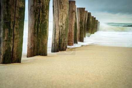 Téléchargez les photos : Brise-vagues sur la plage de Domburg aux Pays-Bas. Photo longue exposition avec des vagues dynamiques se brisant sur le rivage sur des poteaux en bois - en image libre de droit