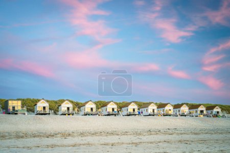 Pequeñas cabañas contra una hilera de dunas con un hermoso cielo nocturno durante el atardecer en la playa