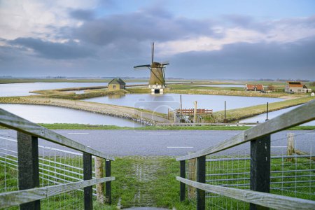 Windmill as water pumping station in Dutch polder with water reservoir and polder landscape view