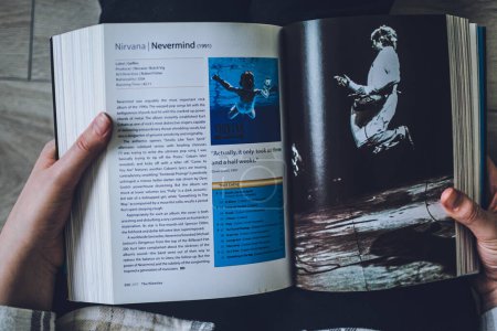 Téléchargez les photos : Lviv, Ukraine - 7 avril 2023 : Une fille lisant "1001 albums que vous devez entendre avant de mourir", passe en revue certains des meilleurs albums de l'histoire de l'industrie musicale. Une page sur le Nirvana et leur disque "Nevermind". - en image libre de droit