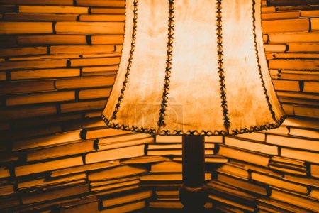 Foto de Lámpara antigua que ilumina libros apilados en las paredes con luz amarilla cálida. Sala de lectura fondo interior - Imagen libre de derechos