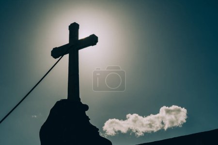 Die Silhouette eines Steinkreuzes gegen den strahlenden Himmel