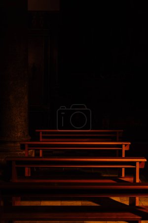 Schattiges Interieur einer Kathedrale in Italien. Ein Rohbau aus Holzbänken im Dunkeln.