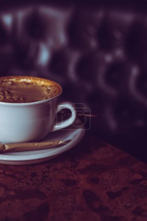 Una taza de café de pie sobre una mesa de estilo vintage. Cappucino fresco con un palo de azúcar. Ambiente acogedor cafetería.