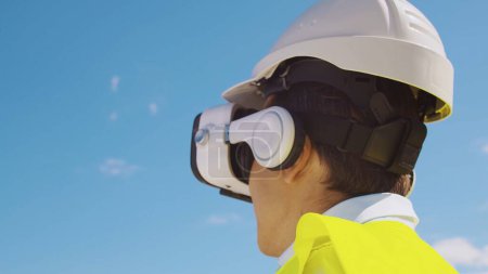 Téléchargez les photos : Constructeur professionnel en casque VR debout devant le chantier de construction et en utilisant des technologies de réalité virtuelle et augmentée. Bâtiment de bureaux et fond de grue. Immobilier et concepts d'investissement - en image libre de droit