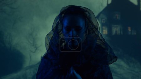Beautiful witch making the witchcraft over the smoky background at night. Scary house on the hill. Halloween image concept.