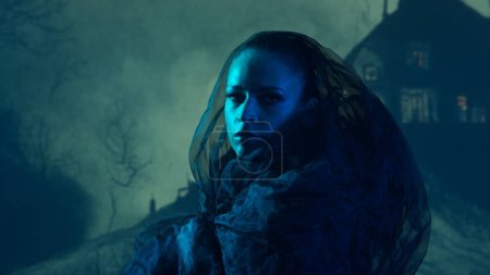 Schöne Hexe, die die Hexerei über dem rauchigen Hintergrund in der Nacht macht. Gruseliges Haus auf dem Hügel. Imagekonzept für Halloween.