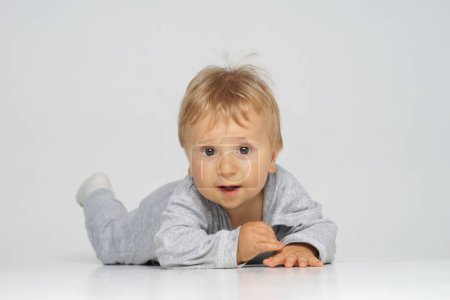 Kleines, glückliches und lächelndes süßes Baby im Studio. Porträt eines einjährigen Babys. Grauer Hintergrund. Das Konzept des Glücks.