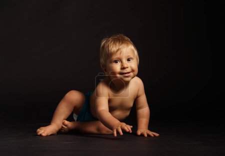 Téléchargez les photos : Petit, heureux et souriant bébé mignon dans le studio. Portrait d'un bébé d'un an. Fond noir. Le concept de bonheur. - en image libre de droit