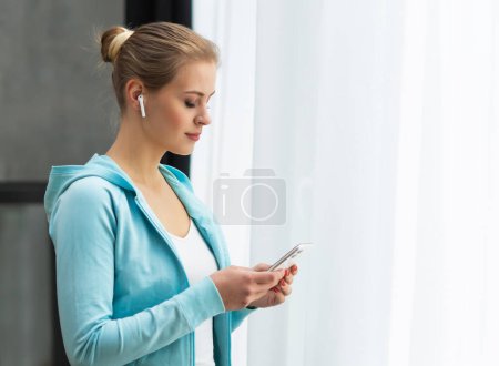 Téléchargez les photos : Close-up portrait of young woman standing in front of the window and looking into it. Girl at home in the living room. Morning concept. - en image libre de droit