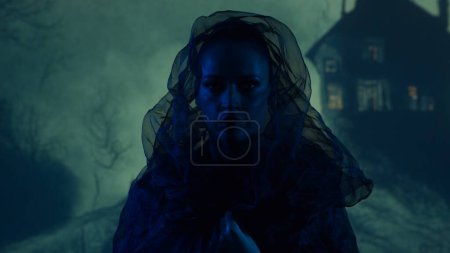 Téléchargez les photos : Belle sorcière faisant la sorcellerie sur le fond fumé la nuit. Maison effrayante sur la colline. Concept d'image Halloween. - en image libre de droit