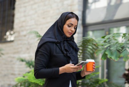 Téléchargez les photos : Close-up portrait of young and attractive muslim woman in hijab. Middle Eastern woman outdoor on the street. City background. The concept of business. - en image libre de droit
