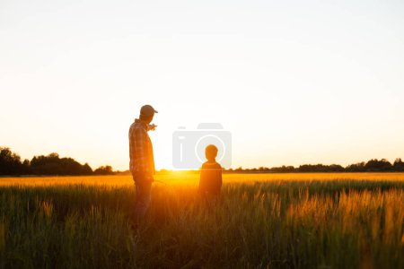 Farmer and his son in front of a sunset agricultural landscape. Man and a boy in a countryside field. The concept of fatherhood, country life, farming and country lifestyle.