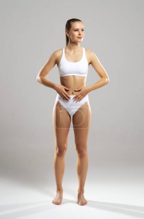 Foto de Young, fit and beautiful blond woman in white swimsuit isolated on grey background. The concept of healthcare, diet, sport and fitness. - Imagen libre de derechos