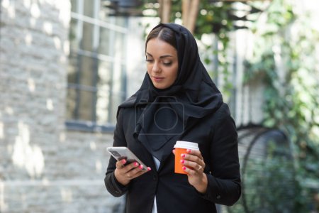 Téléchargez les photos : Close-up portrait of young and attractive muslim woman in hijab. Middle Eastern woman outdoor on the street. City background. The concept of business. - en image libre de droit