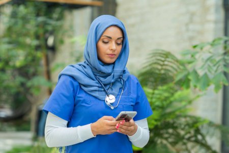 Téléchargez les photos : Close-up portrait of young and attractive muslim woman nurse in hijab. Middle Eastern female doctor outdoor on the street. City background. The concept of medicine and health care. - en image libre de droit