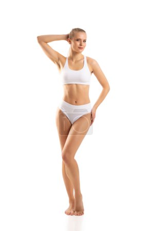 Foto de Young, fit and beautiful blond woman in white swimsuit isolated on grey background. The concept of healthcare, diet, sport and fitness. - Imagen libre de derechos