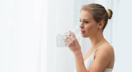 Foto de Close-up portrait of young woman standing in front of the window and looking into it. Girl at home in the living room. Morning concept. - Imagen libre de derechos