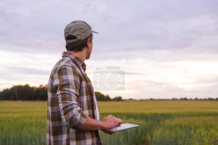 Photo for Farmer with a tablet computer in front of a sunset agricultural landscape. Man in a countryside field. The concept of country life, food production, farming and technology. - Royalty Free Image