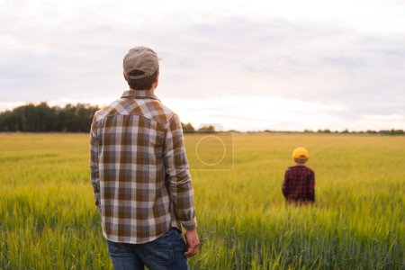 Téléchargez les photos : Farmer and his son in front of a sunset agricultural landscape. Man and a boy in a countryside field. The concept of fatherhood, country life, farming and country lifestyle. - en image libre de droit