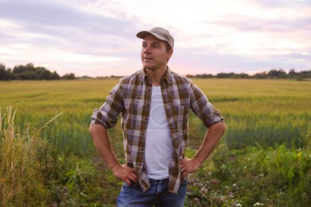 Téléchargez les photos : Farmer in front of a sunset agricultural landscape. Man in a countryside field. The concept of country life, food production, farming and country lifestyle. - en image libre de droit