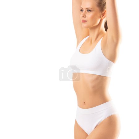 Téléchargez les photos : Jeune et belle fille mince en maillot de bain blanc posant sur fond blanc. Le concept de santé, d'alimentation, de sport et de fitness. - en image libre de droit