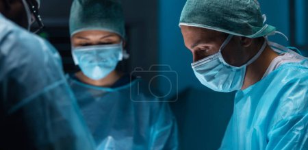 Diverse team of professional medical doctors performs a surgical operation in a modern operating room using high-tech equipment and technology. Surgeons are working to save the patient in the hospital. Medicine, health and science concept.