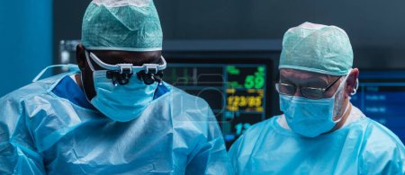 Téléchargez les photos : Une équipe diversifiée de médecins professionnels effectue une opération chirurgicale dans une salle d'opération moderne à l'aide d'équipements et de technologies de pointe. Les chirurgiens travaillent pour sauver le patient à l'hôpital - en image libre de droit