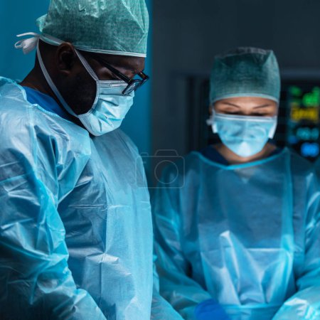 Foto de Diverso equipo de médicos profesionales realiza una operación quirúrgica en un quirófano moderno utilizando equipos y tecnología de alta tecnología. Los cirujanos están trabajando para salvar al paciente en el hospital. - Imagen libre de derechos