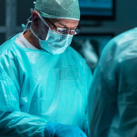 Téléchargez les photos : Une équipe diversifiée de médecins professionnels effectue une opération chirurgicale dans une salle d'opération moderne à l'aide d'équipements et de technologies de pointe. Les chirurgiens travaillent pour sauver le patient à l'hôpital - en image libre de droit