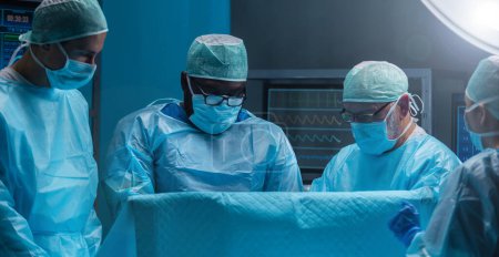 Photo for Diverse team of professional medical doctors performs a surgical operation in a modern operating room using high-tech equipment and technology. Surgeons are working to save the patient in the hospital - Royalty Free Image