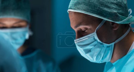 Diverse team of professional medical doctors performs a surgical operation in a modern operating room using high-tech equipment and technology. Surgeons are working to save the patient in the hospital