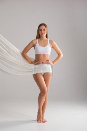 Téléchargez les photos : Young, fit and beautiful blond woman in white swimsuit isolated on grey background. The concept of healthcare, diet, sport and fitness. - en image libre de droit