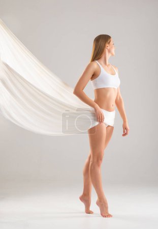 Téléchargez les photos : Young, fit and beautiful blond woman in white swimsuit isolated on grey background. The concept of healthcare, diet, sport and fitness. - en image libre de droit