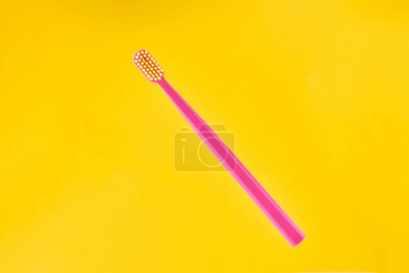 Téléchargez les photos : Pink toothbrush on yellow background for oral hygiene to clean teeth, gums and tongue. Manual plastic toothbrush for effective toothbrushing and healthy smile, isolated on yellow background - en image libre de droit