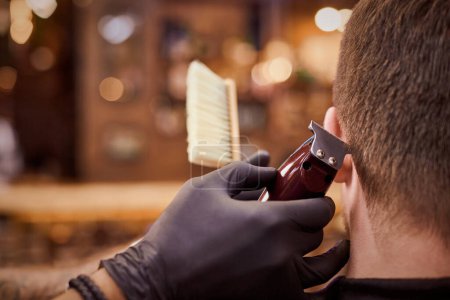 Foto de Male haircut trimming in barbershop, client getting haircut by hairdresser with clipper and hairbrush. Hairdresser makes hairdo in hairdresser salon, new stylish modern haircut for man - Imagen libre de derechos