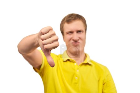 Téléchargez les photos : Unhappy annoyed man in yellow T-shirt showing thumbs down gesture isolated on white background. Dissatisfied customer with dislike hand gesture, disappointed displeased man - en image libre de droit