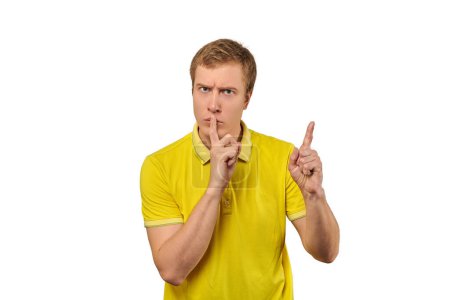 Téléchargez les photos : Funny male in yellow T-shirt asking to be quiet, silence gesture isolated on white background. Young man saying Shhh, keep quiet, please and making silence gesture, request for silence - en image libre de droit