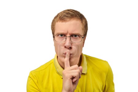 Téléchargez les photos : Funny young man in yellow T-shirt asking to be quiet, silence gesture isolated on white background. Young man in glasses saying Shhh, keep quiet, please and making silence gesture, request for silence - en image libre de droit