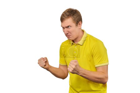 Téléchargez les photos : Aggressive angry man in yellow T-shirt looking to left and ready to fight with fists isolated on white background. Annoyed young man ready to fight, defense gesture, left copy space - en image libre de droit