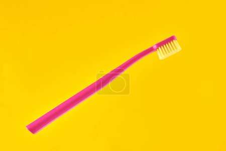 Téléchargez les photos : Pink toothbrush on yellow background for oral hygiene to clean teeth, gums and tongue. Manual plastic toothbrush for effective toothbrushing and healthy smile, isolated on yellow background - en image libre de droit