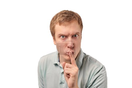 Téléchargez les photos : Funny guy in light gray Polo T-shirt asking to be quiet, silence gesture isolated on white background. Young man saying Shhh, keep quiet, please and making silence gesture, request for silence - en image libre de droit