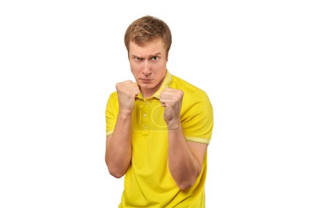 Photo for Angry young man in yellow T-shirt ready to fight with fists isolated on white background. Confident handsome man going to attack in fistfight, defense gesture, aggressive man with clenched fists - Royalty Free Image
