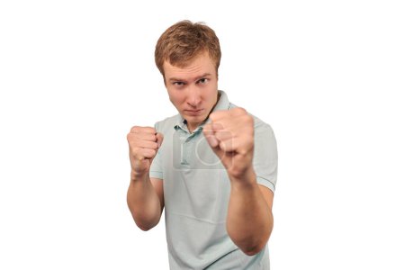 Téléchargez les photos : Angry young man in light grey T-shirt ready to fight with fists isolated on white background. Aggressive handsome man going to fistfight, defense gesture, bad guy with clenched fists - en image libre de droit